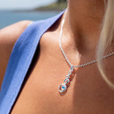A detailed close-up of the Silver Origins stacked pebble and blue topaz pendant on a sterling silver chain, worn on a woman's neck.